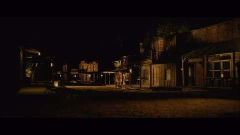 Old Western town buildings with wood facades and windows at night, dimly lit by lanterns and street lights, creating a vintage scene.