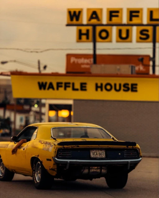 Yellow vintage car parked near a Waffle House restaurant, captured in an eye-level medium shot under soft, diffused natural light.
