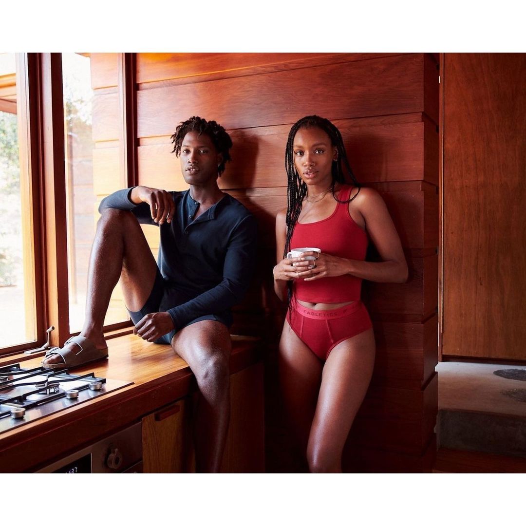 A relaxed indoor shot of a man in a long-sleeved shirt and shorts sitting next to a woman in matching top and underwear.