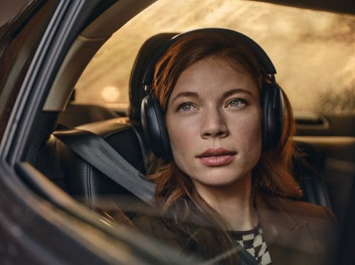 Woman wearing headphones in a car with a seatbelt, looking out the window with soft focus and natural lighting.