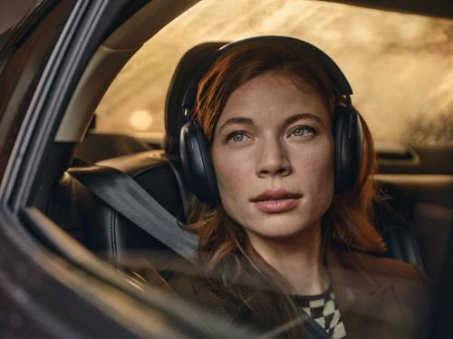 Woman wearing headphones in a car with a seatbelt, looking out the window with soft focus and natural lighting.