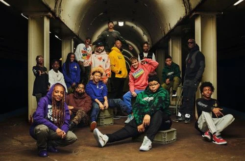 Group of diverse people in colorful casual clothing gather in an urban tunnel underpass with concrete pillars and muted lighting.