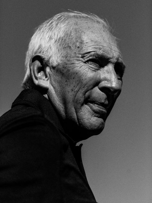 Portrait of an elderly man with short white hair and weathered skin in profile against an open sky.