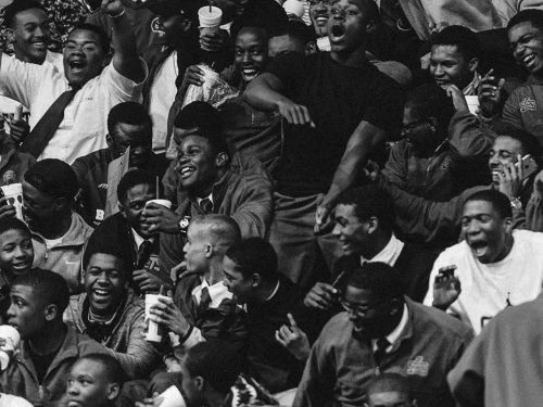 Enthusiastic crowd of predominantly Black spectators cheer, captured in a black and white photograph showcasing a moment of collective excitement.