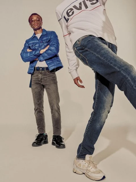 Two people in a fashion shot. One person stands at full length wearing a blue puffer jacket and jeans. The second person is cropped.