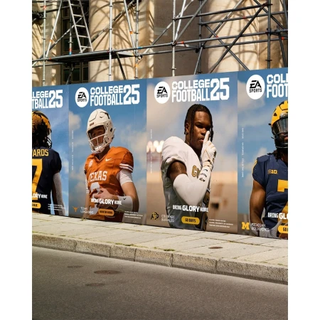 Four 'EA Sports College Football 25' advertisements featuring football players in uniform are displayed on a city street corner.