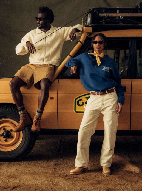 Two adults, one male and one female, pose next to a yellow vehicle in outdoor shot, wearing casual attire and sunglasses.