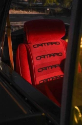 Close-up interior view of a bright red velour car seat with repeated Camaro embroidery, shot by Nicholas Maggio.