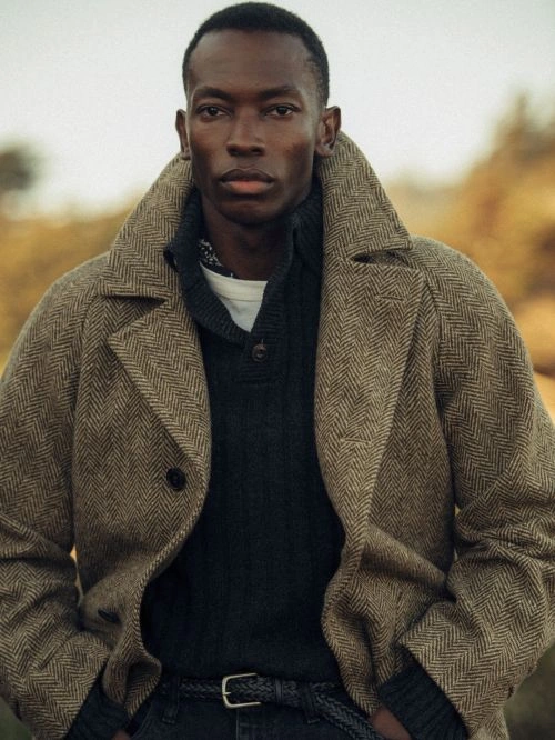 Portrait of a Black man wearing a herringbone coat over a dark knit sweater photographed by Nicholas Maggio