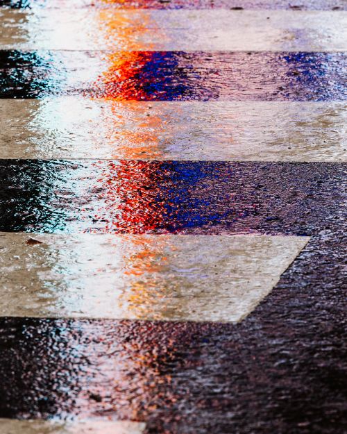Abstract wet zebra crossing on pavement with reflections of blue and red lights, creating an interesting street scene.