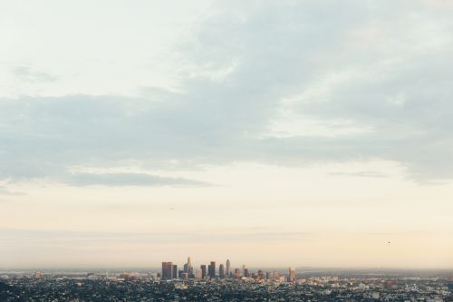 Cityscape view of Los Angeles with skyscrapers, buildings, and natural light under a cloudy sky during the daytime.