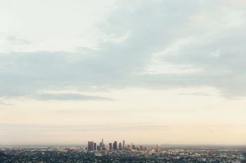 Cityscape view of Los Angeles with skyscrapers, buildings, and natural light under a cloudy sky during the daytime.