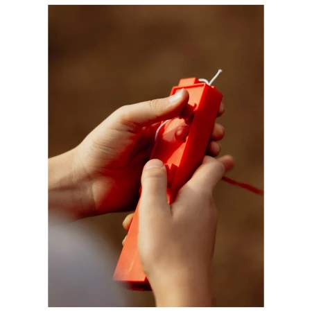 Close-up shot of a child's hands holding a bright orange toy with string outdoors in soft, natural light with blurred background.