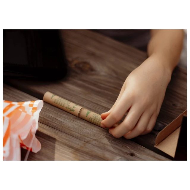 Child's hand near a cylindrical container on a wooden picnic table, next to a partially visible food wrapper and a cardboard box.