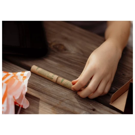 Child's hand near a cylindrical container on a wooden picnic table, next to a partially visible food wrapper and a cardboard box.