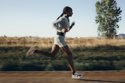A long-distance runner races through an open field on a sunny day, capturing motion blur on the landscape, clothing, and the runner's legs.