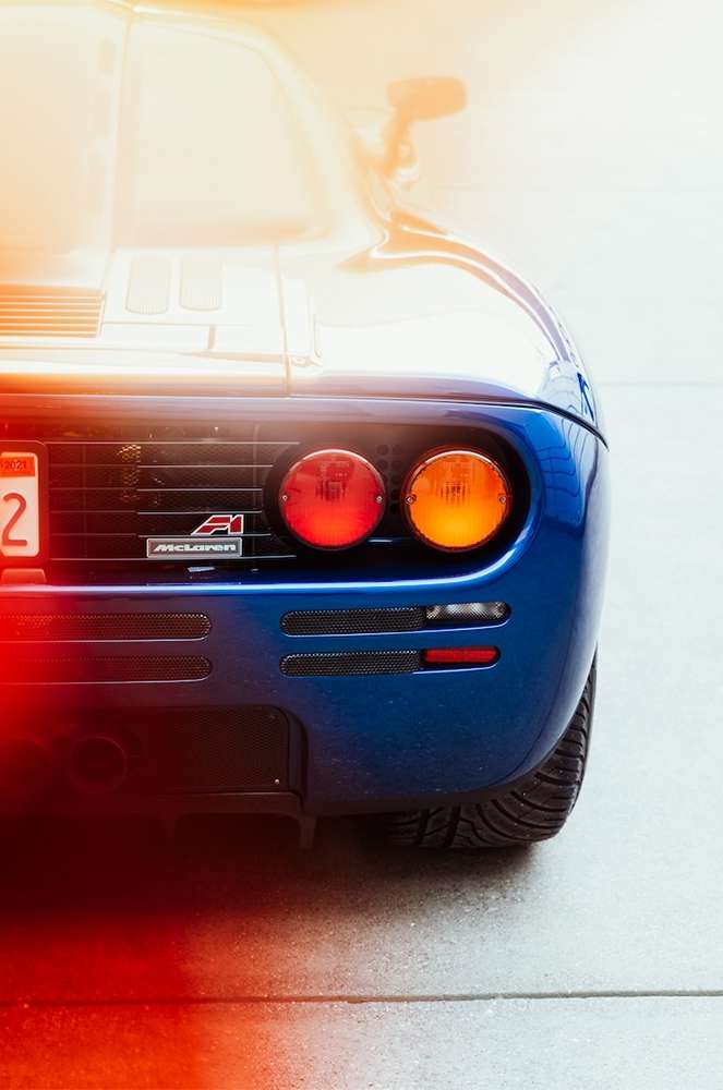 Rear view of a blue McLaren F1 car showcasing its taillights, exhaust, and sleek design on a concrete surface. Automotive photography.