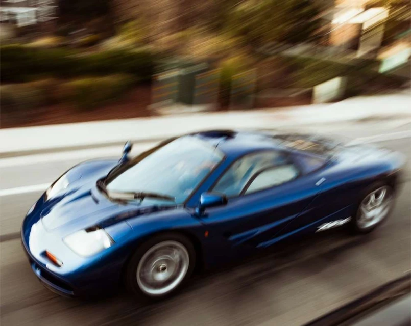 High-speed view of a blue McLaren F1 supercar on a city street, using motion blur to convey velocity and power.