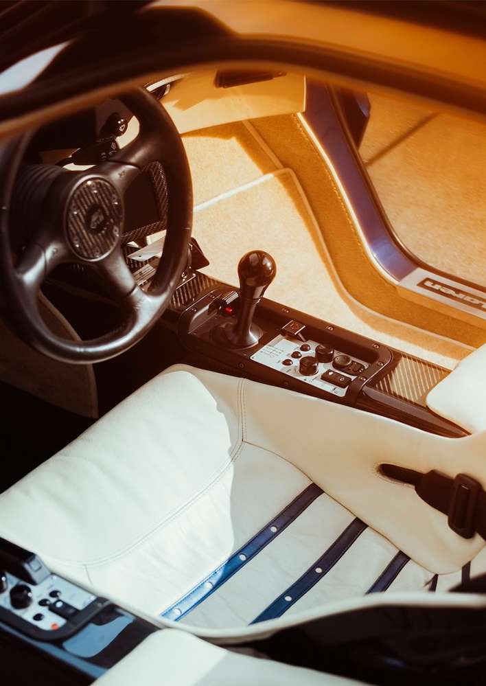 Interior view of a luxury car with a steering wheel, ivory leather seat with blue accents, and a sleek, modern design aesthetic.