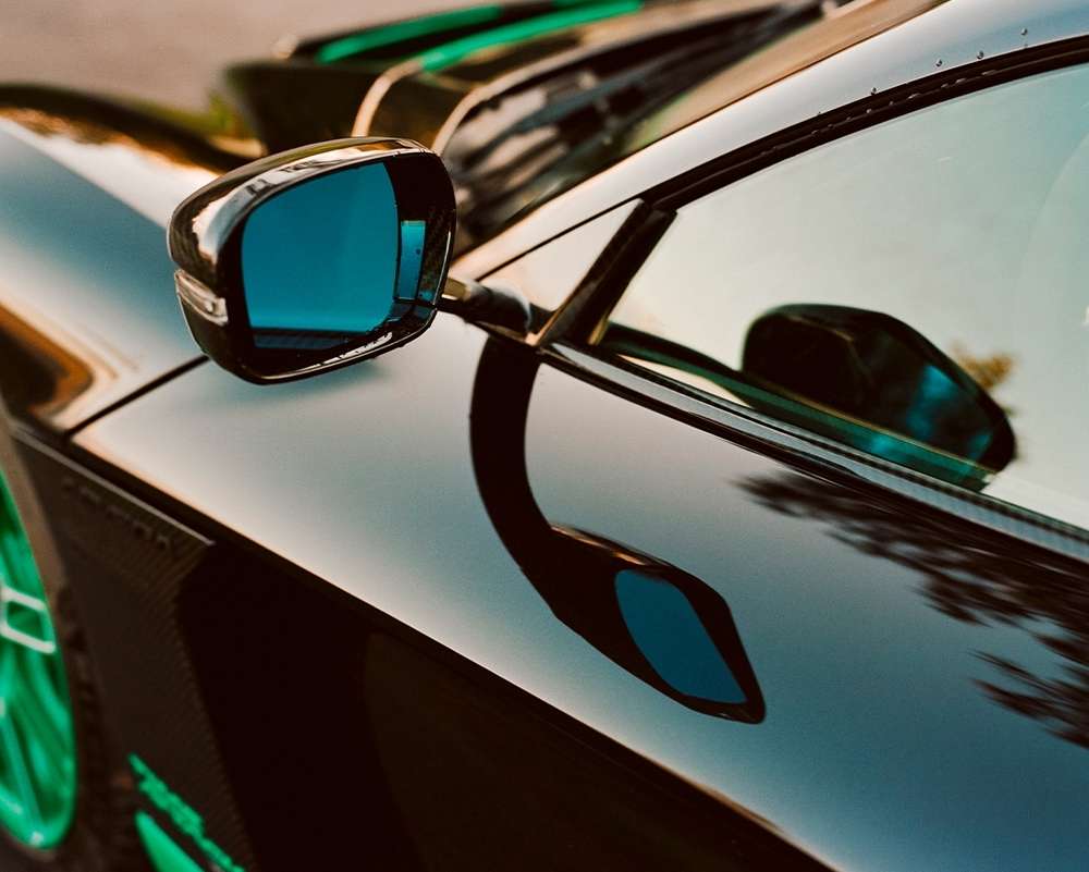 Close-up of a sleek, dark sports car featuring a glossy finish, reflective side mirrors, and vibrant green accents on the wheels and trim.