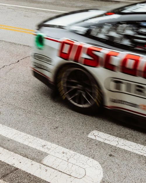 Blurred motion shot of a race car on asphalt racetrack with red Discount Tire livery and yellow lane divider lines on the road surface.