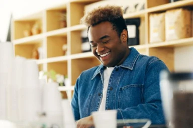 A smiling black man wearing a blue denim jacket in a cafe interior captured by Kennett Mohrman.