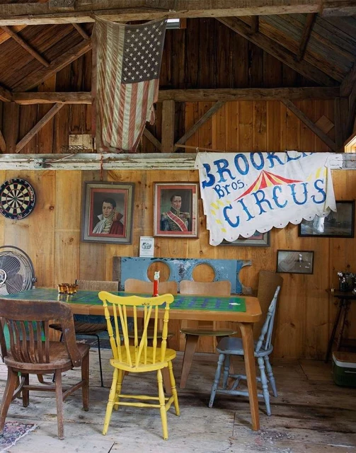 Indoor scene with a wooden table surrounded by chairs, an American flag, circus banner, and portraits on the wood-paneled wall.