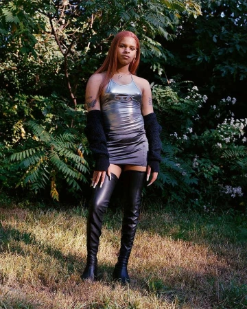 Model with long reddish hair wearing a metallic silver minidress and black leather thigh-high boots outdoors