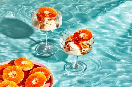 Two stem glasses filled with ice cream, tangerine slices, and nuts on a patterned blue surface with citrus fruit pieces.