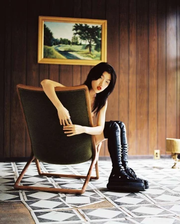 Woman in tall black boots seated backward on an armchair against wood-paneled walls by Fumi Nagasaka