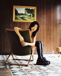 Woman in tall black boots seated backward on an armchair against wood-paneled walls by Fumi Nagasaka