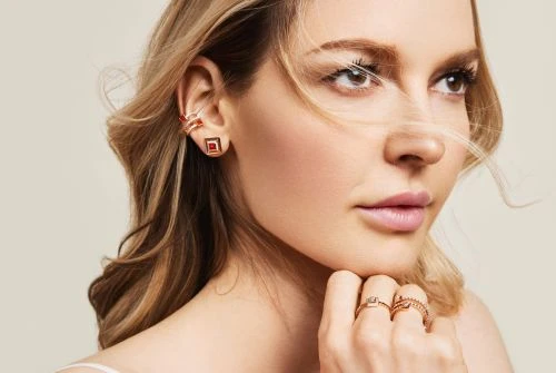 Close-up beauty portrait of a woman wearing gold jewellery including rings, square earrings, and an ear cuff, with make-up by Sophie Ono.