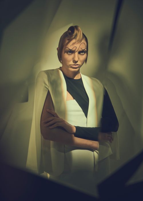 Fashionable woman with creative makeup and modern hairstyle in a white cape in a studio with geometric lighting.