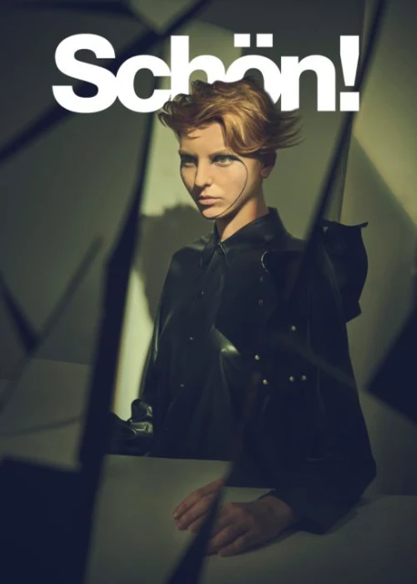 Magazine cover featuring a person with short blond hair, a dark shirt, and geometric background shapes. The magazine's name is "Schön!".