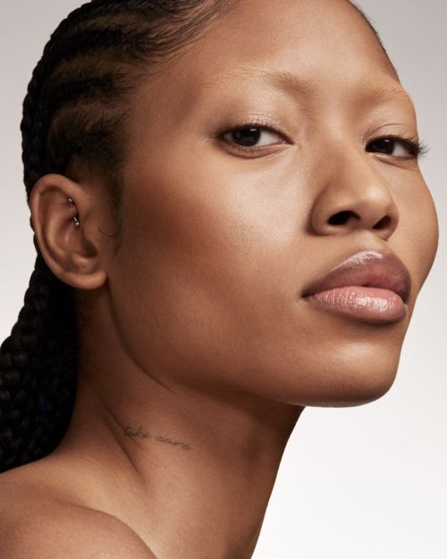 Close-up portrait of a woman with braids, natural makeup, and glossy lips against a neutral background for beauty and fashion concepts.