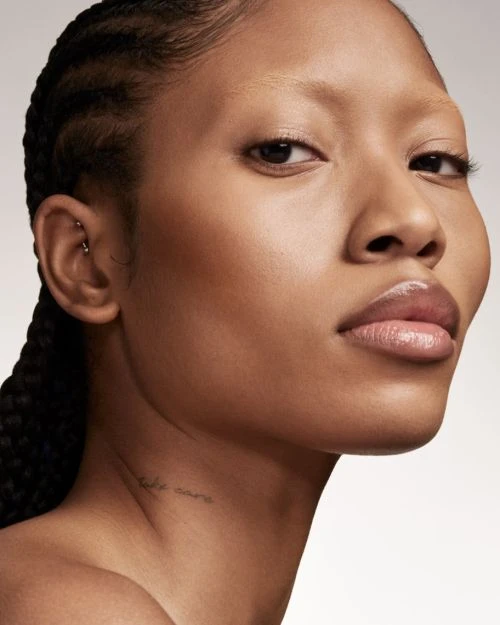 Close-up portrait of a woman with braids, natural makeup, and glossy lips against a neutral background for beauty and fashion concepts.