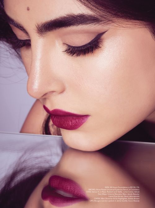 Close-up portrait of a woman with dark hair, focused on her makeup: defined eyeliner, full brows, and deep berry lipstick.