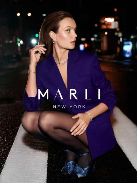 Stunning woman in a purple blazer and jewelry crouches on a crosswalk at night in an urban setting, promoting Marli New York jewelry.