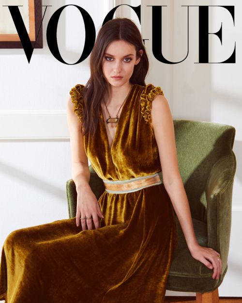 Portrait of a dark-haired woman in a mustard-colored velvet dress on a green chair, as seen on a Vogue magazine cover.
