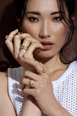 Close-up of an Asian woman showcasing multiple gold rings on her fingers against a blurred background, jewelry focused in frame.