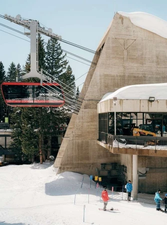 Red Snowbird ski lift ascends mountain at resort with skiers and snowboarders visible in snow covered landscape on a bright day.