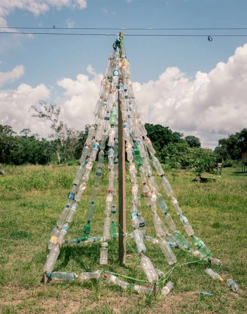 Recycled plastic bottle tree structure in a grassy outdoor field under a bright sky with scattered clouds.