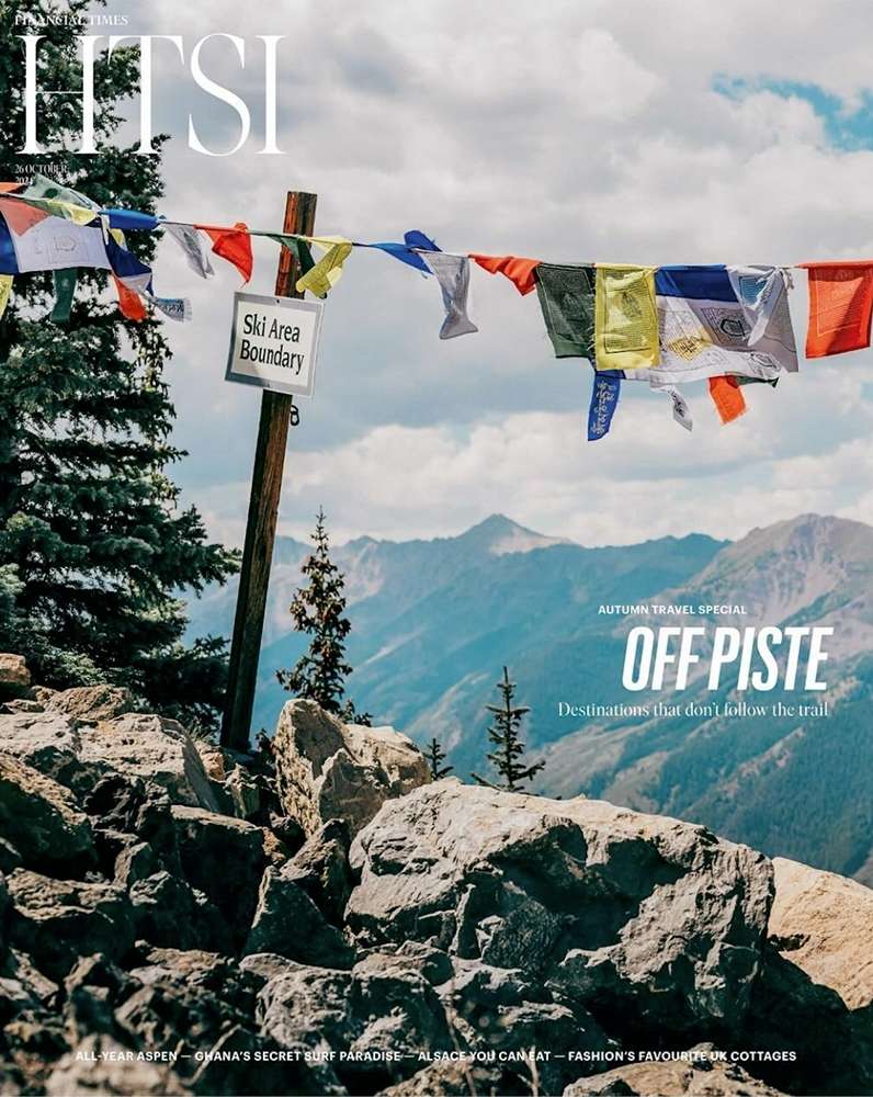 Magazine cover featuring a mountain landscape and colorful prayer flags strung across a ski area boundary sign on a rocky mountaintop.