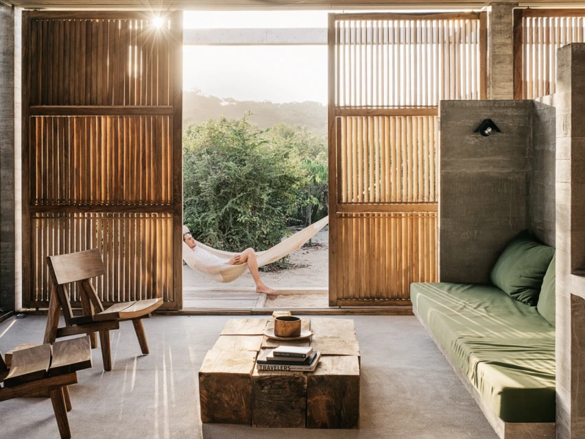 Man relaxing in hammock, open-air architectural space with wooden details and a lush green view, bathed in natural light.