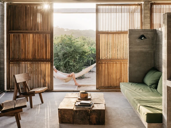 Man relaxing in hammock, open-air architectural space with wooden details and a lush green view, bathed in natural light.