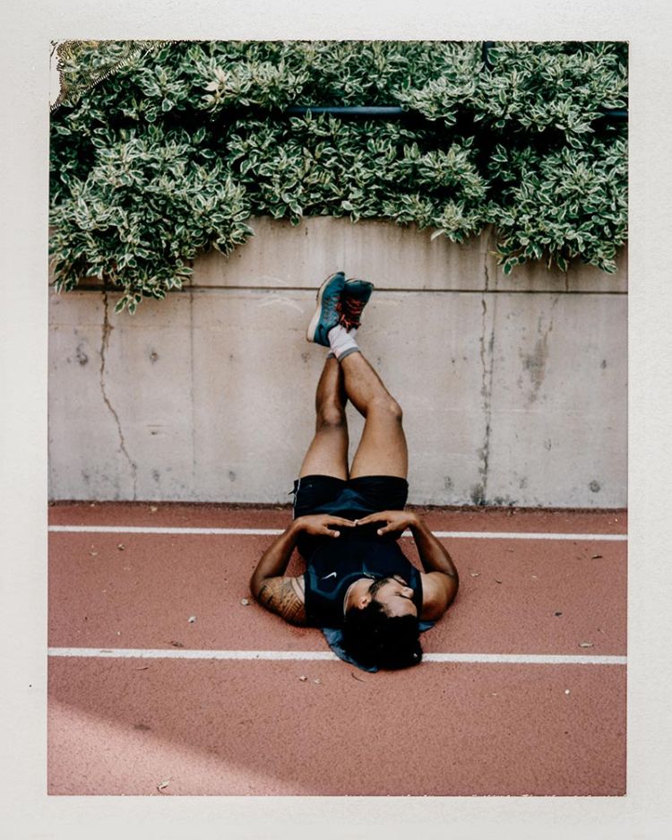 Man lying on a running track with legs resting up against a concrete wall under green foliage