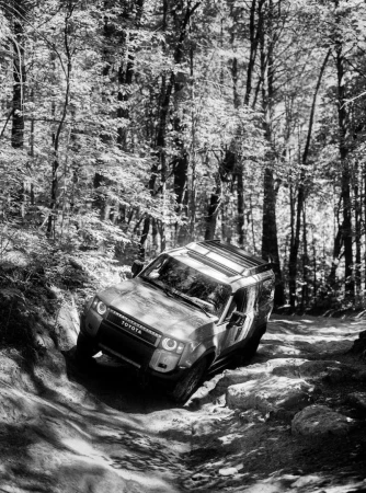 Off-road vehicle, Toyota, drives on a rocky path through a forest. Black and white image with trees surrounding the vehicle.
