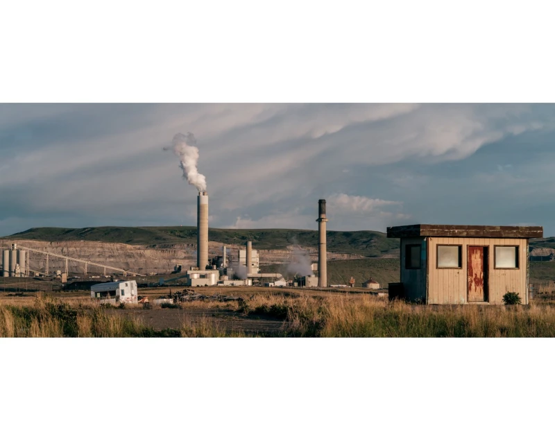 Industrial landscape featuring a power plant with smokestacks emitting steam, captured on a partly cloudy day near a small building.