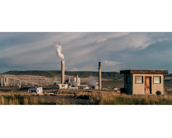 Industrial landscape featuring a power plant with smokestacks emitting steam, captured on a partly cloudy day near a small building.