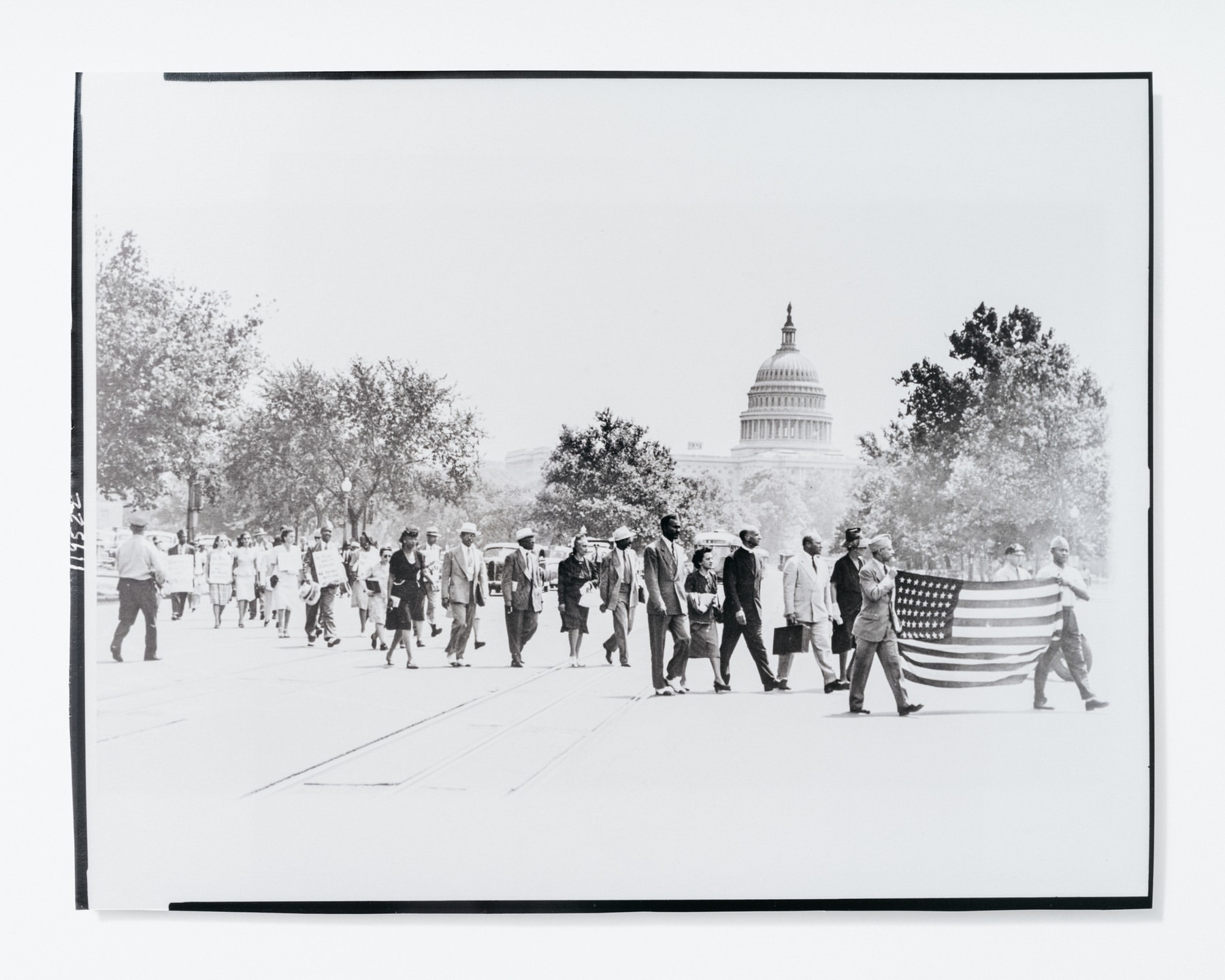 Black and white photograph of a large group of people walking on a street with the United States Capitol building in the background.